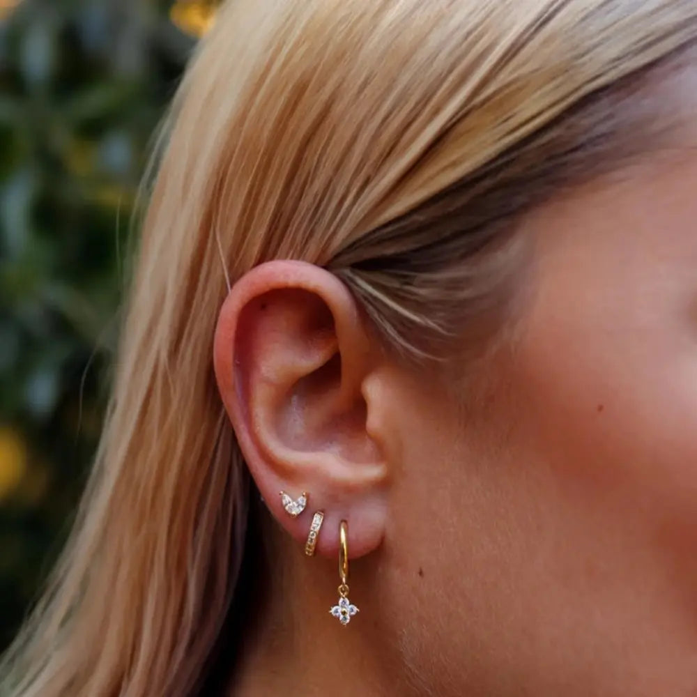 Close-up of a person wearing gold hoop earrings with small diamond-like stones.