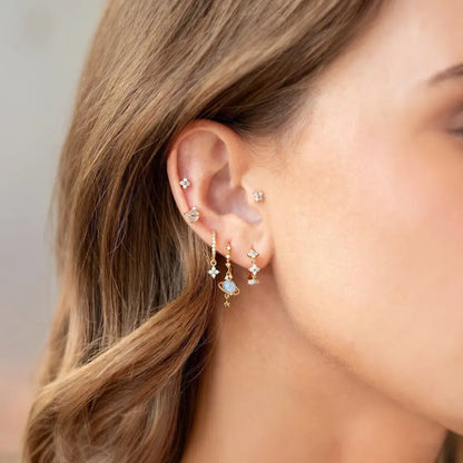 Close-up of a person wearing gold earrings with small gemstones.