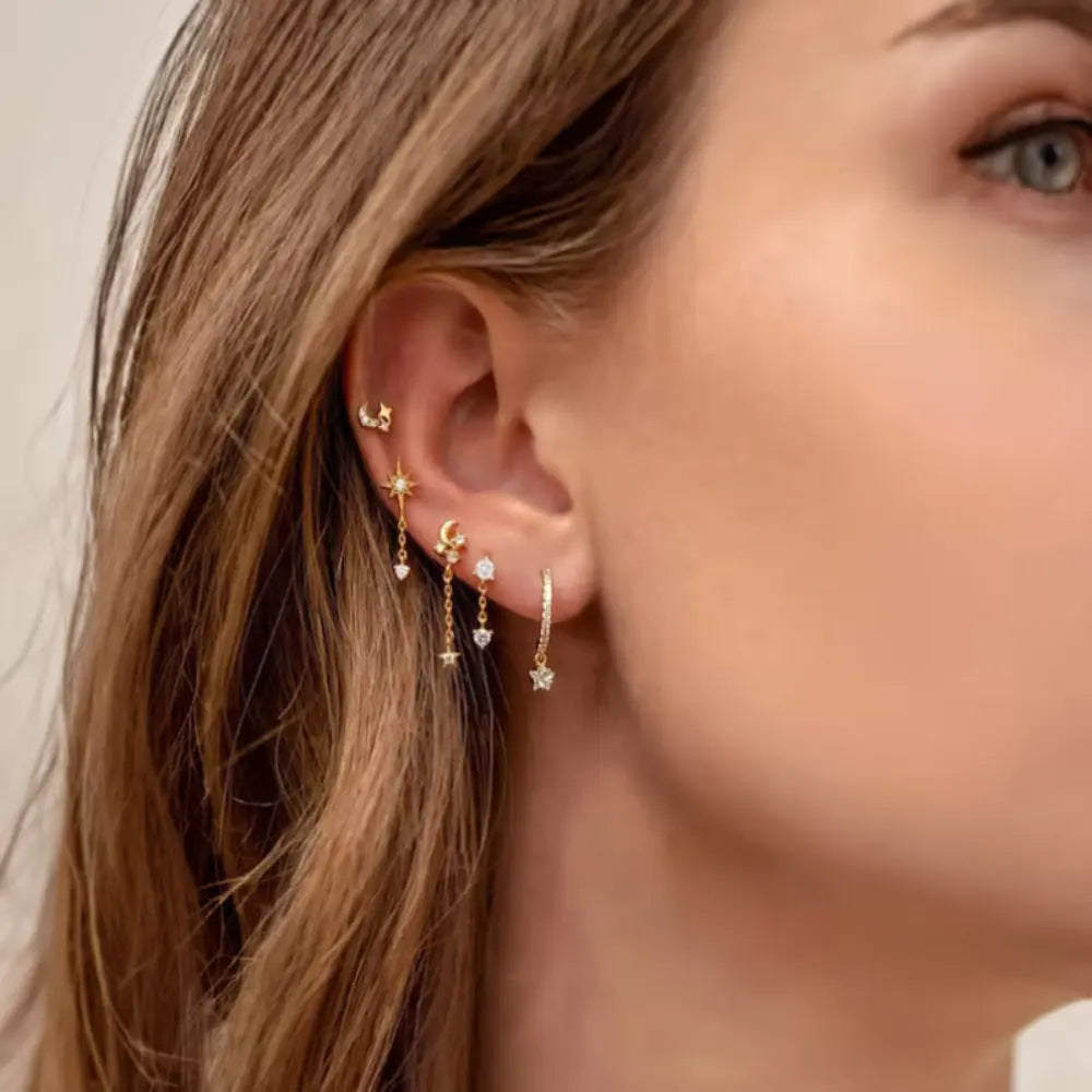 Close-up of a woman's ear wearing gold earrings with small stones.