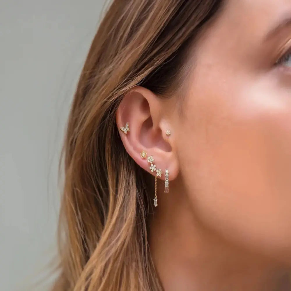 Close-up of an ear with multiple gold earrings against a neutral background
