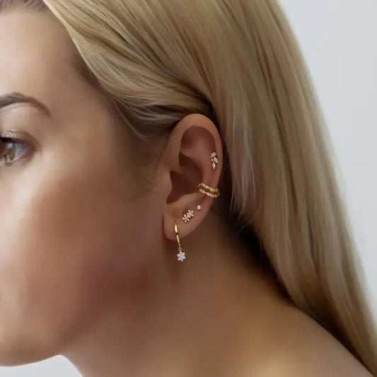 Close-up of a woman's ear wearing gold earrings with a neutral background
