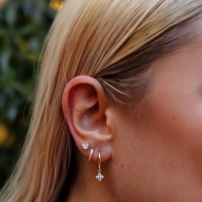 Close-up of a person wearing gold hoop earrings with small diamond-like stones.
